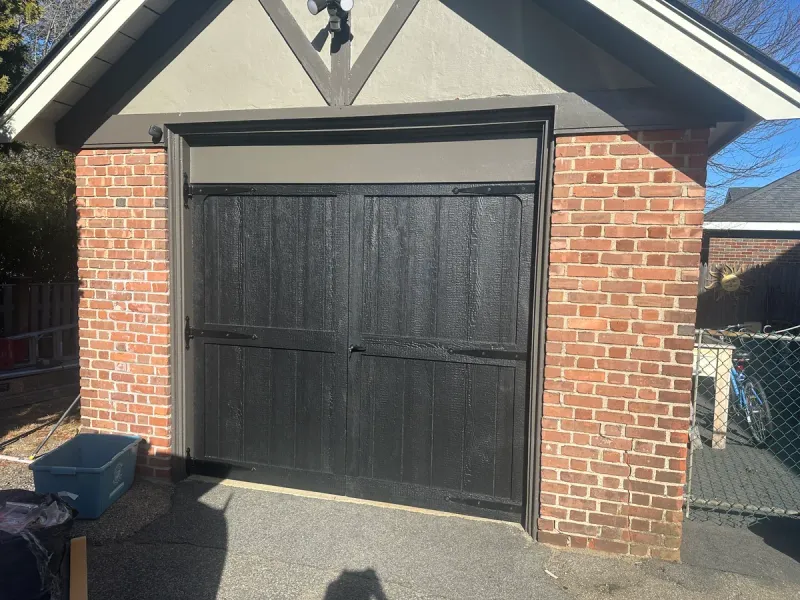Black carriage-style garage door with decorative hardware on brick Tudor-style garage