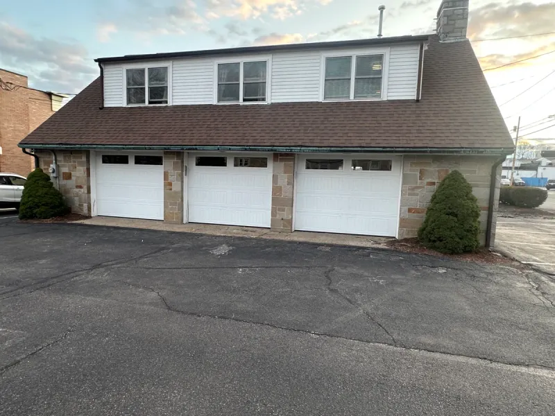 Triple white garage doors with transom windows on stone-faced commercial building