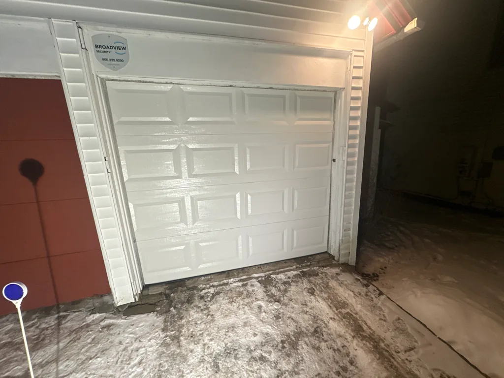 White panel garage door on detached garage illuminated at night in snow